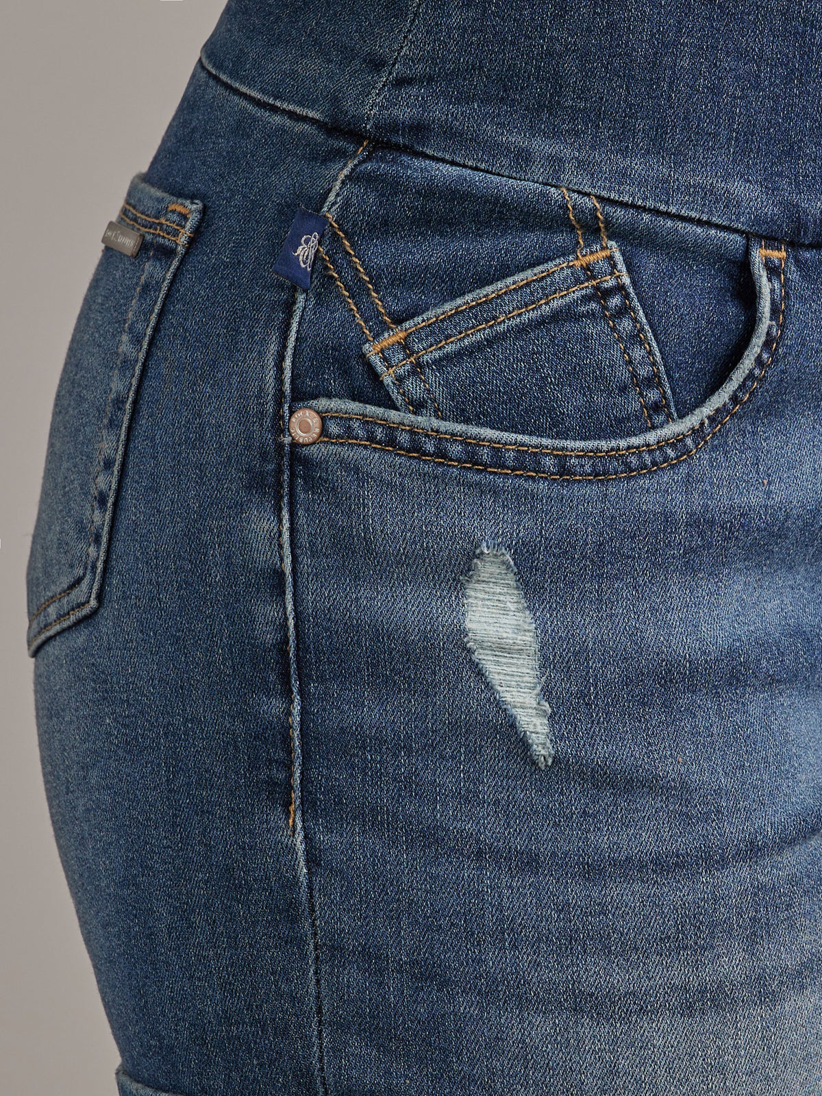 Front pocket detail of Rock & Republic Fever Pull-On Short in Symptomatic with distressed nick and blue woven RR logo tab
