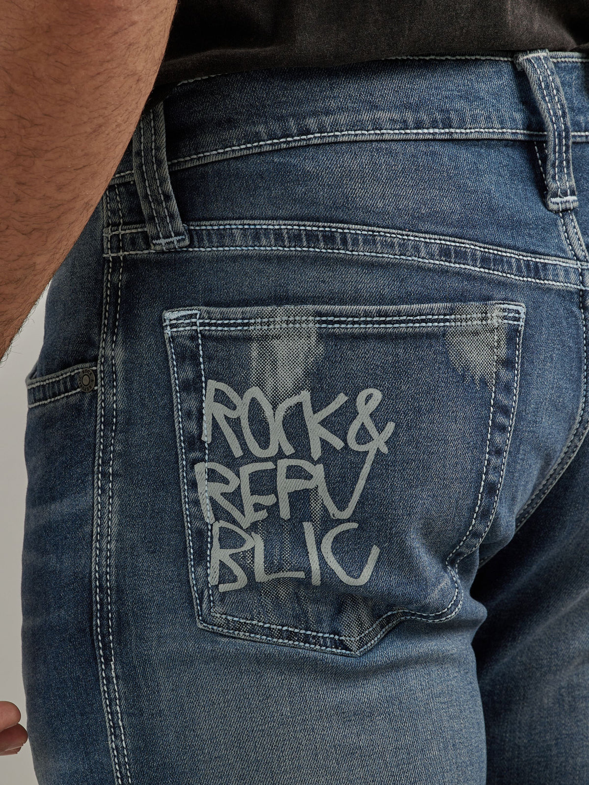 Detailed back pocket view of Rock & Republic Neil jeans in Denied showing hand-drawn Rock & Republic graffiti logo tag.