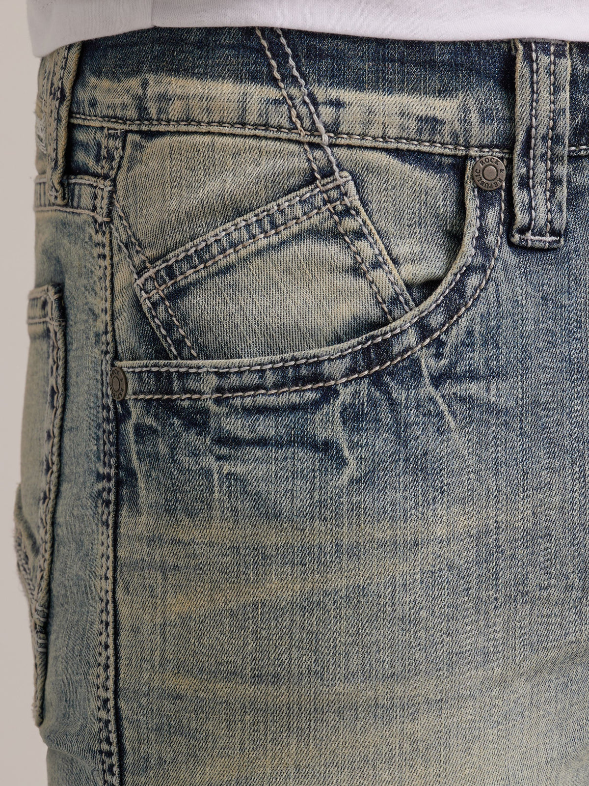 Close-up of Rock & Republic Neil jeans front waist in Haze showing angled coin pocket and warm tint whiskering details.