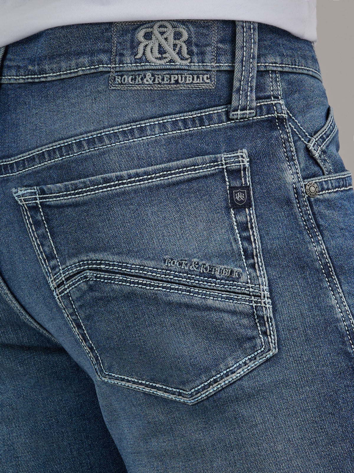 Detailed back pocket view of Rock & Republic Henlee jeans in Denied showing embroidered logo patch and crest logo tab.