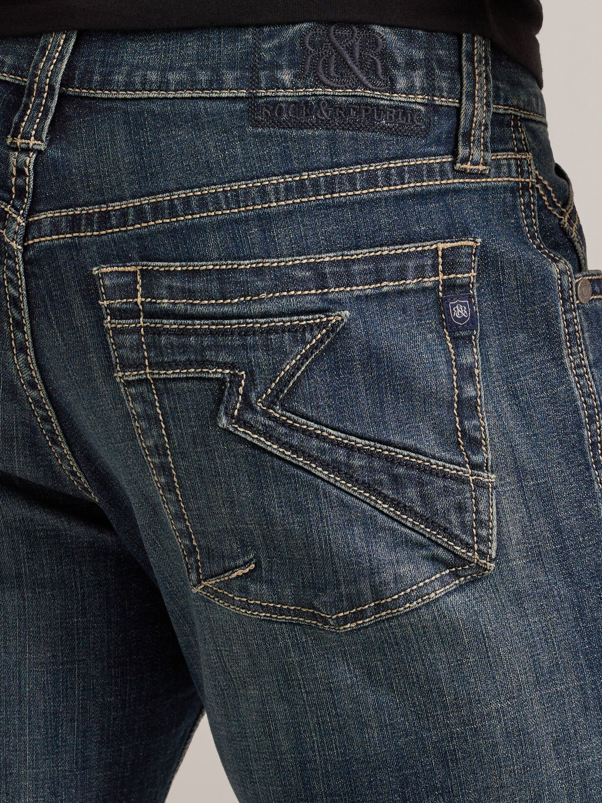 Close-up of Rock & Republic Grady jeans back pocket in Radiator featuring signature tan angular R embroidery and crest tab.