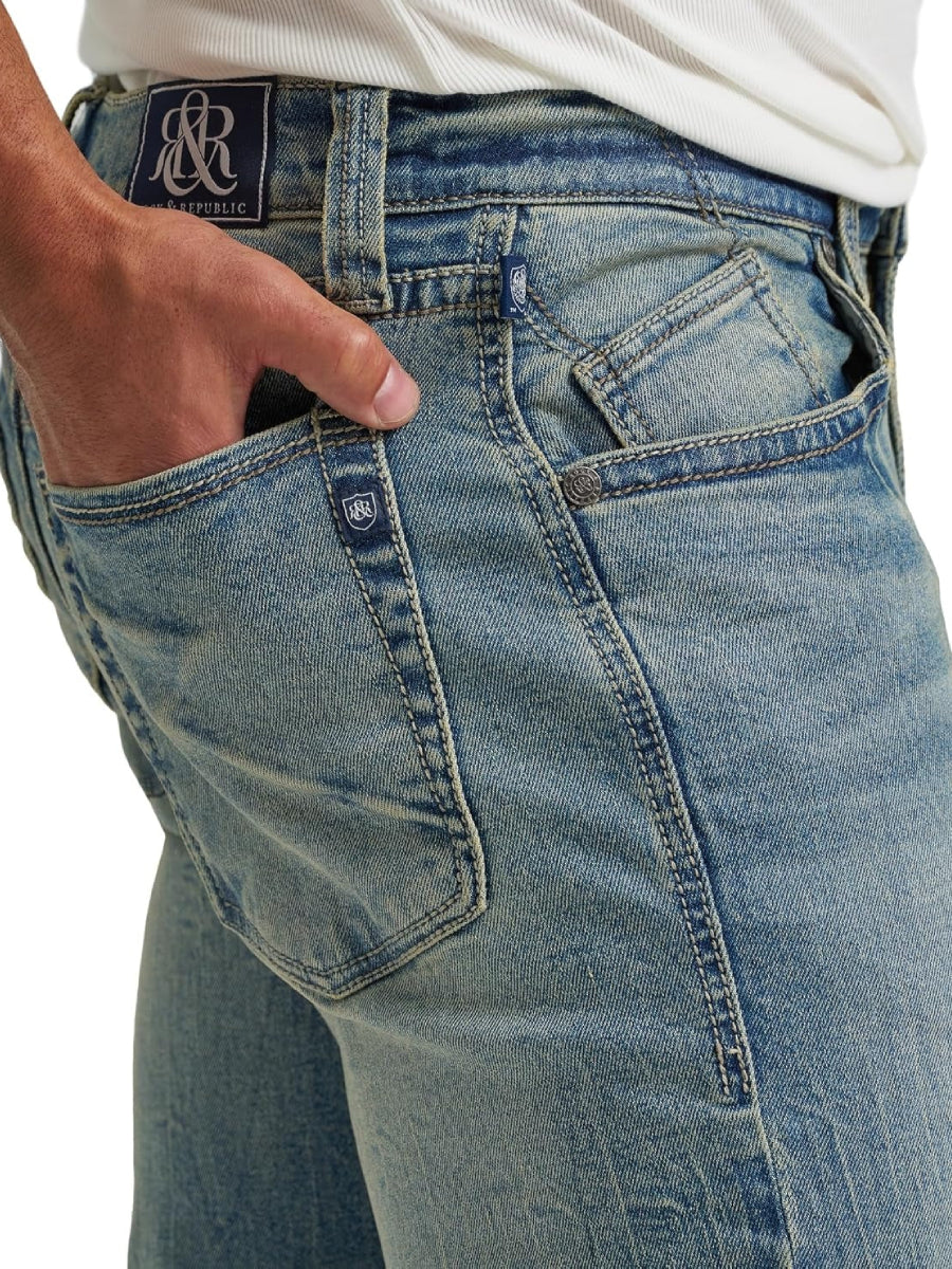 Side waist close-up of Rock & Republic Henlee jeans in Headbanger showing angled forward seam and R&R logo patch detail.