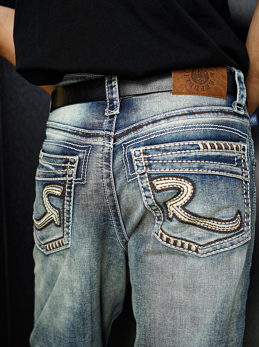 Rear view of Rock & Republic Grady jeans showing embossed leather patch and back pockets with signature tan stitched R logo.