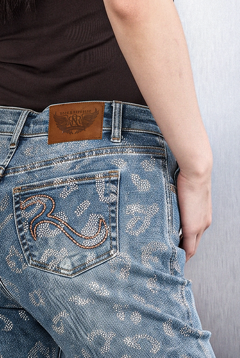 Detailed rear view of Rock & Republic Kaia straight jeans featuring embossed leather logo waistband patch and embroidered pocket.