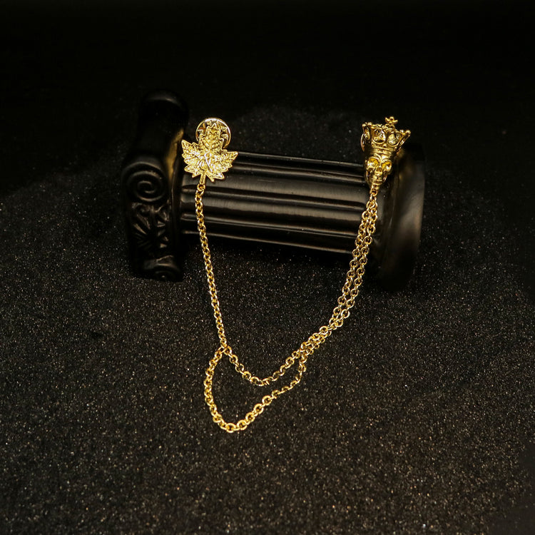 Display view of Rock & Republic Chain-Embellished Brooch in Gold with crowned skull, crystal maple leaf, and double chains.