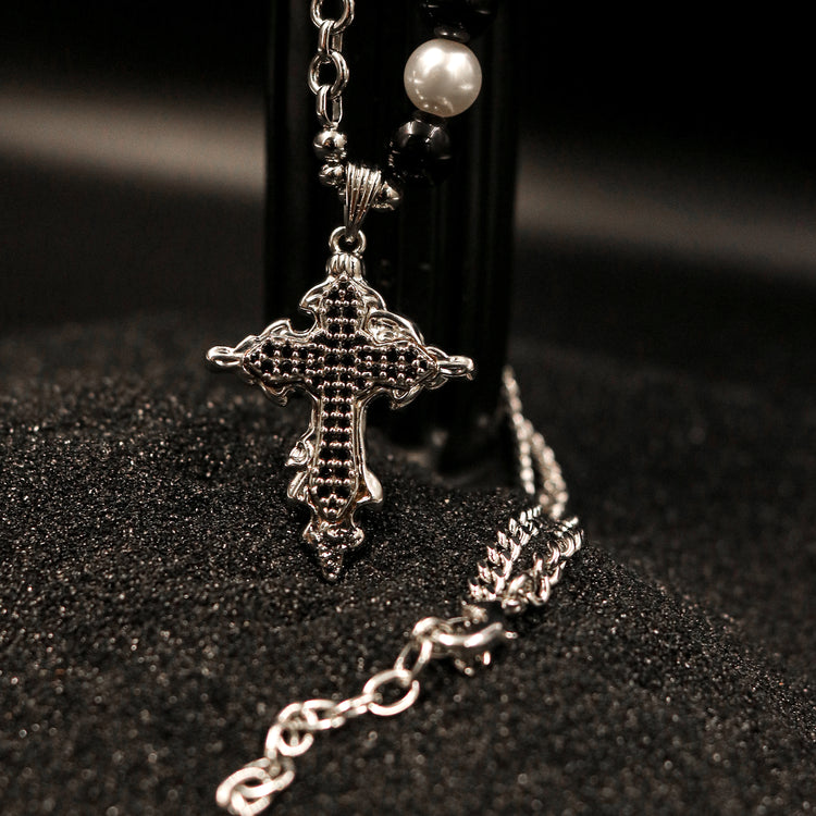 Macro view of Rock & Republic embellished cross pendant necklace in Silver highlighting pavé black stone gothic cross.