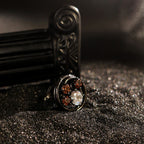 Rock & Republic Cubic Zirconia Cluster Ring in Black copper on dark sand with open circular frame and CZ stone cluster.