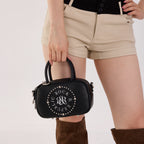 Rock & Republic Studded Logo Medallion Satchel Bag in Black PU held by model showcasing structured satchel body.